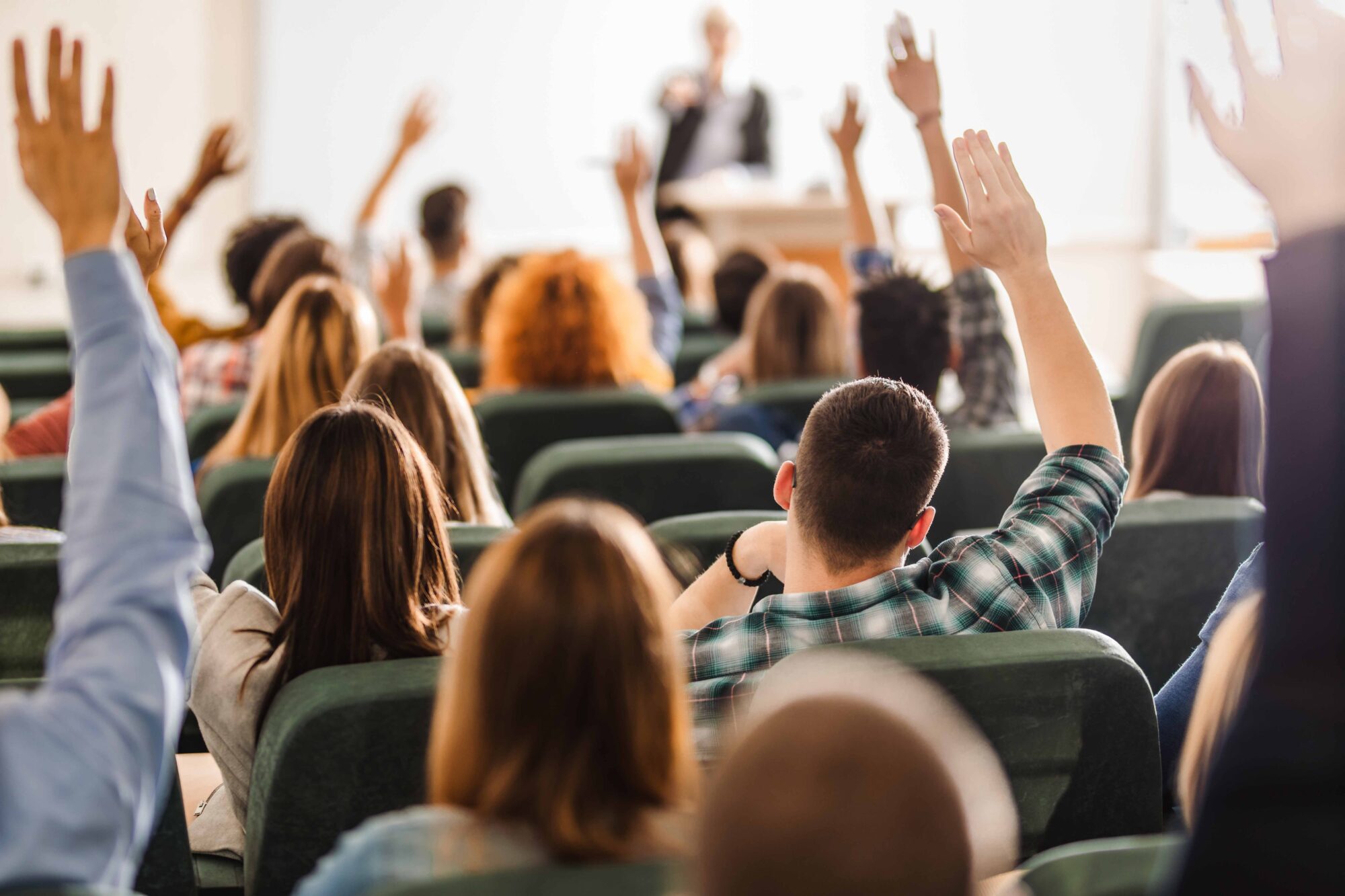 Rear view of large group of students raising arms during a class at amphitheater.