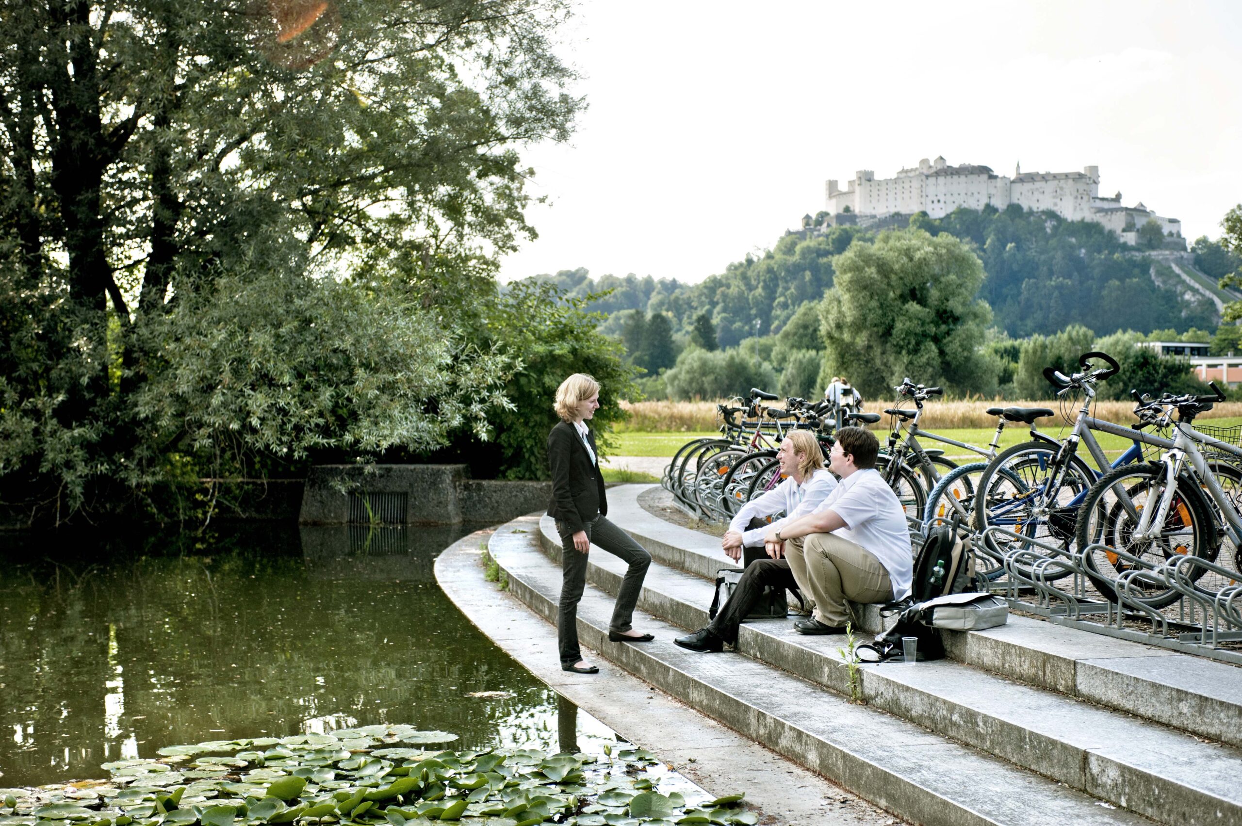 Studierende sitzen auf den Stufen am Wasser, Blick auf die Festung