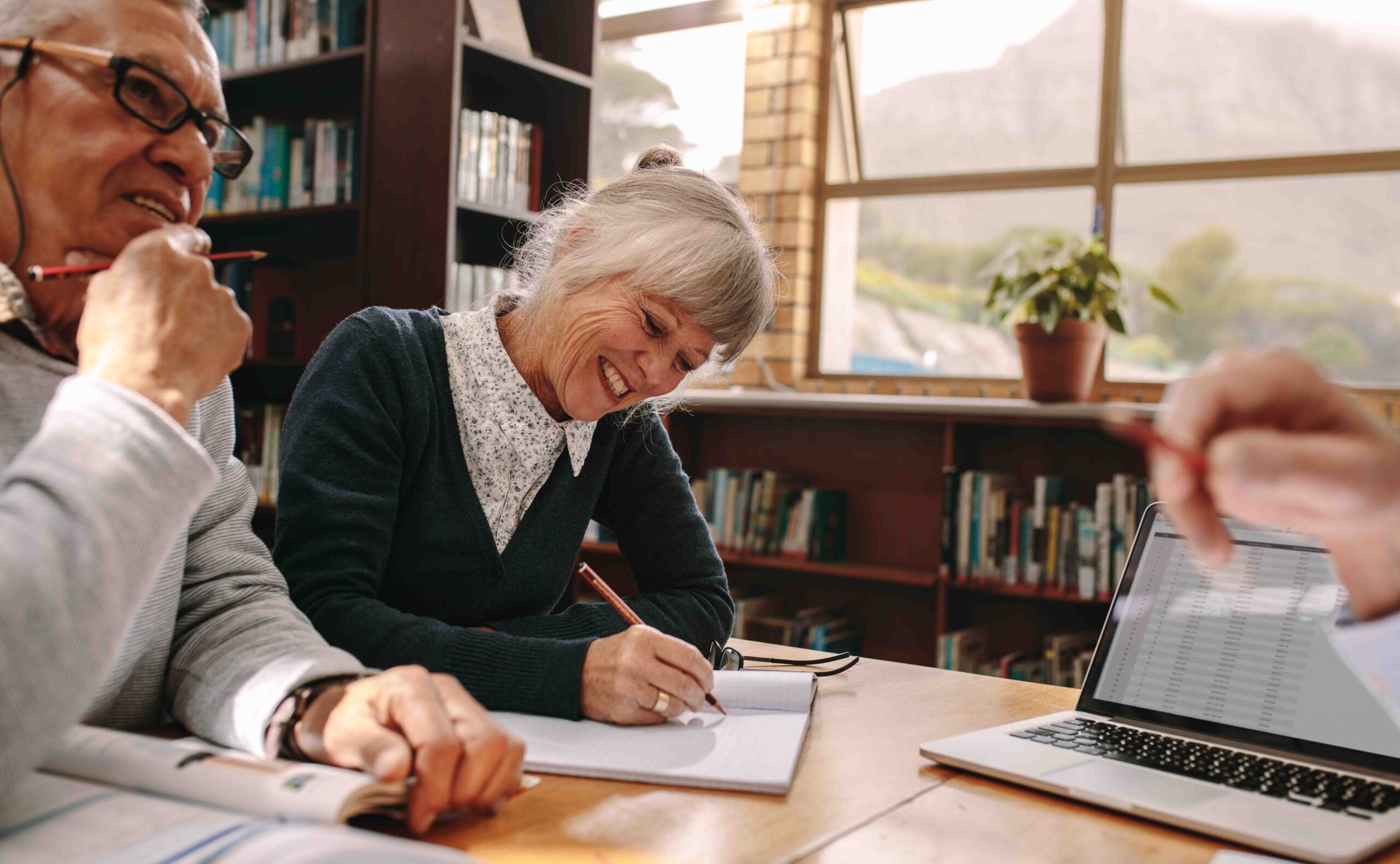 enior woman writing notes sitting in a library with her male colleagues. Elderly people discussing and learning in a university college.