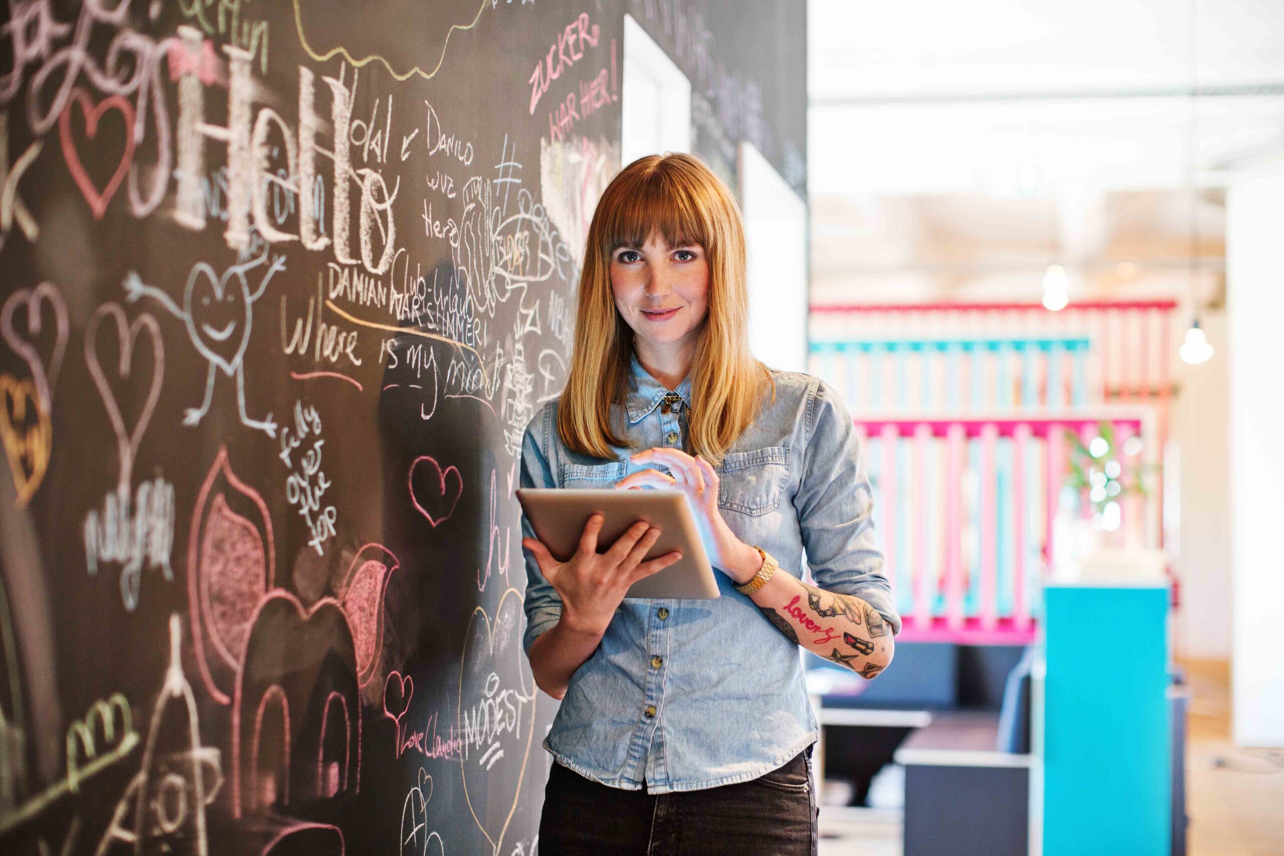 Portrait of beautiful businesswoman using digital tablet in office. Female professional is standing by scribbled blackboard. She is wearing smart casuals at workplace.