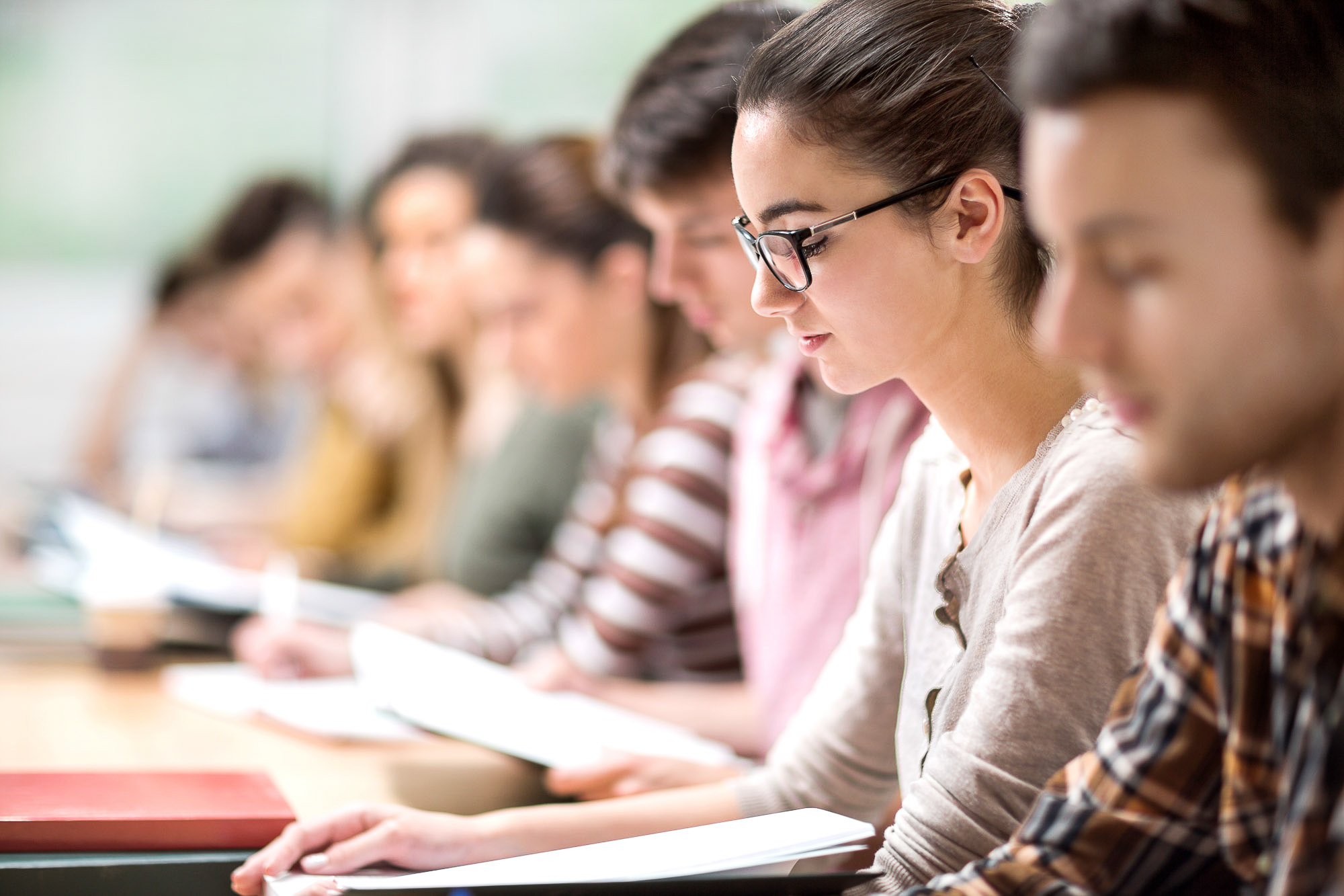 Group of students having a class. Focus is on young woman reading a book.