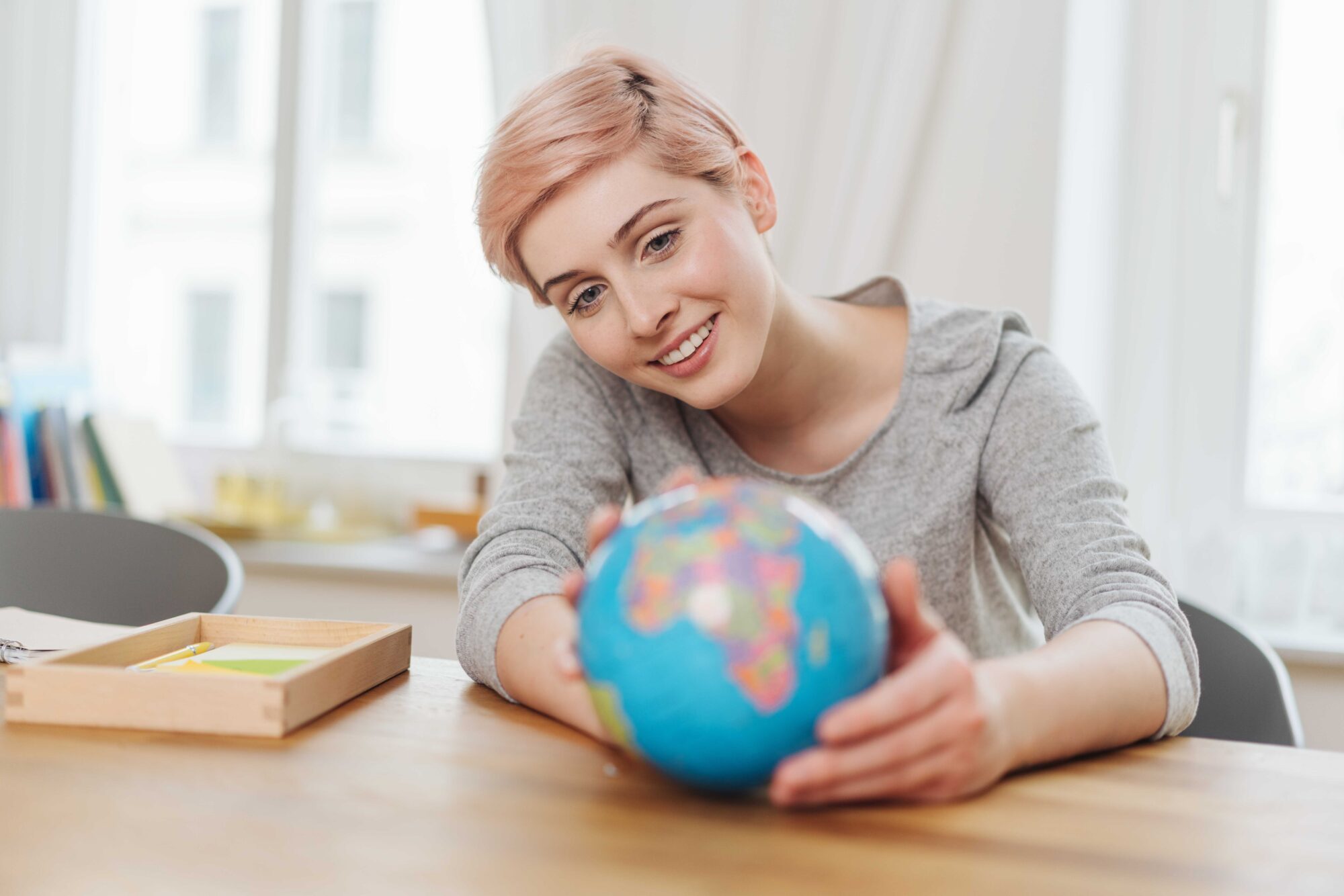 Young woman holding a world globe in her hands on a wooden table as she plans her annual vacation with a happy smile