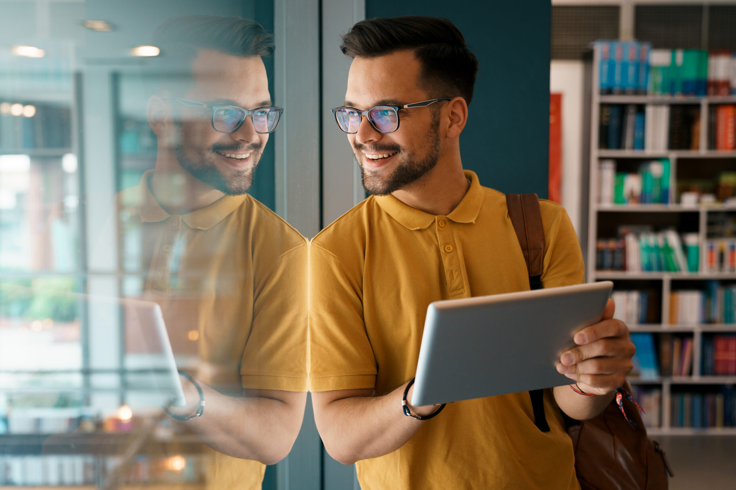 Photo: Young happy college man using digital tablet at the library - Stock Photo