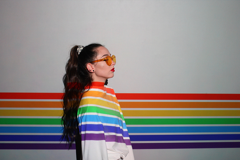 Frau steht vor Wand mit Regenbogen