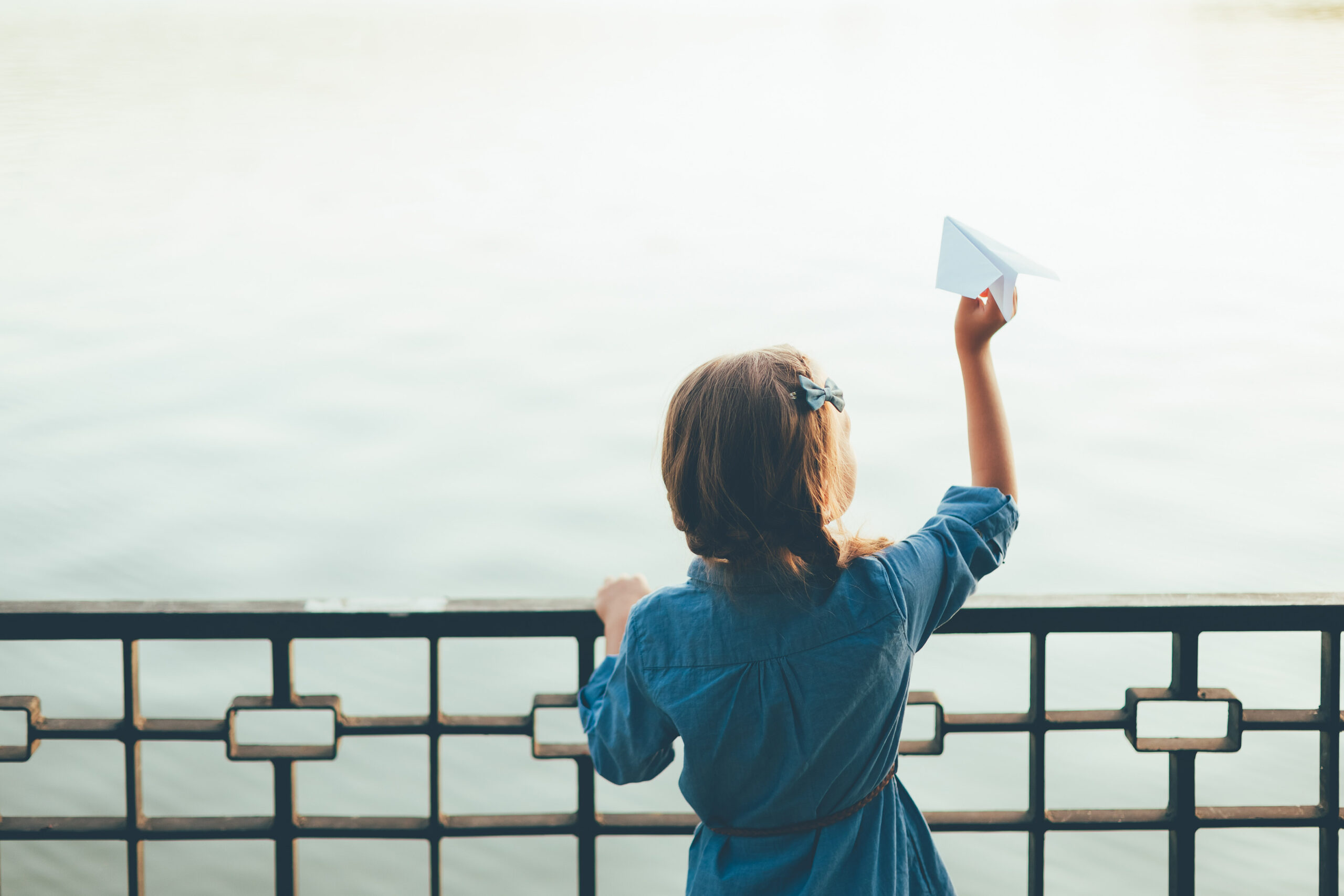 Girl with toy paper airplane looking to lake