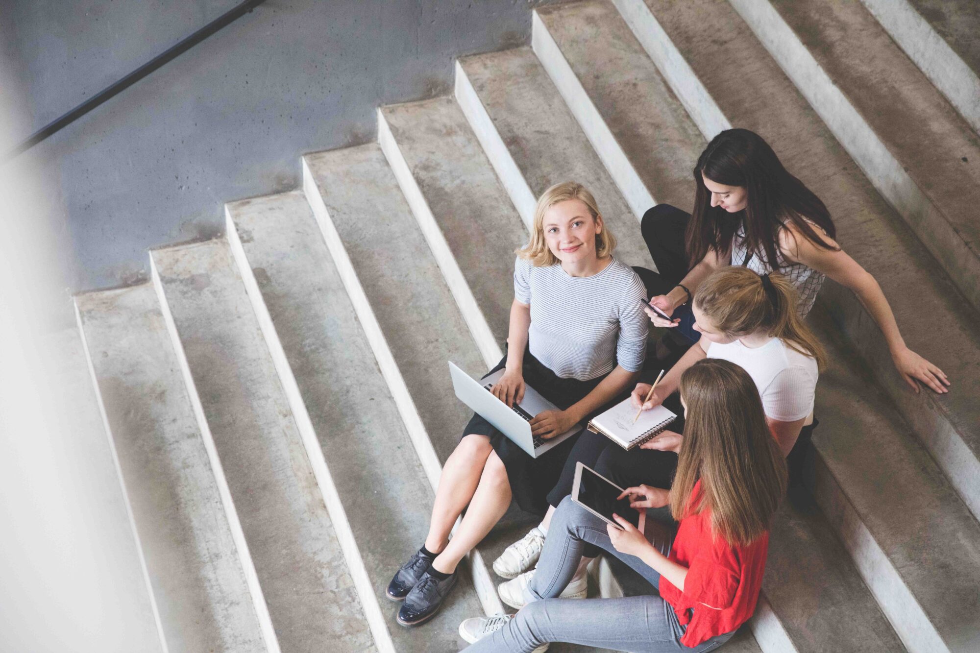 Young and happy urban people holding technologies while sitting on steps