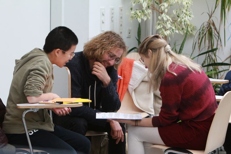drei studierenden sitzen auf stühlen und arbeiten gemeinsam
