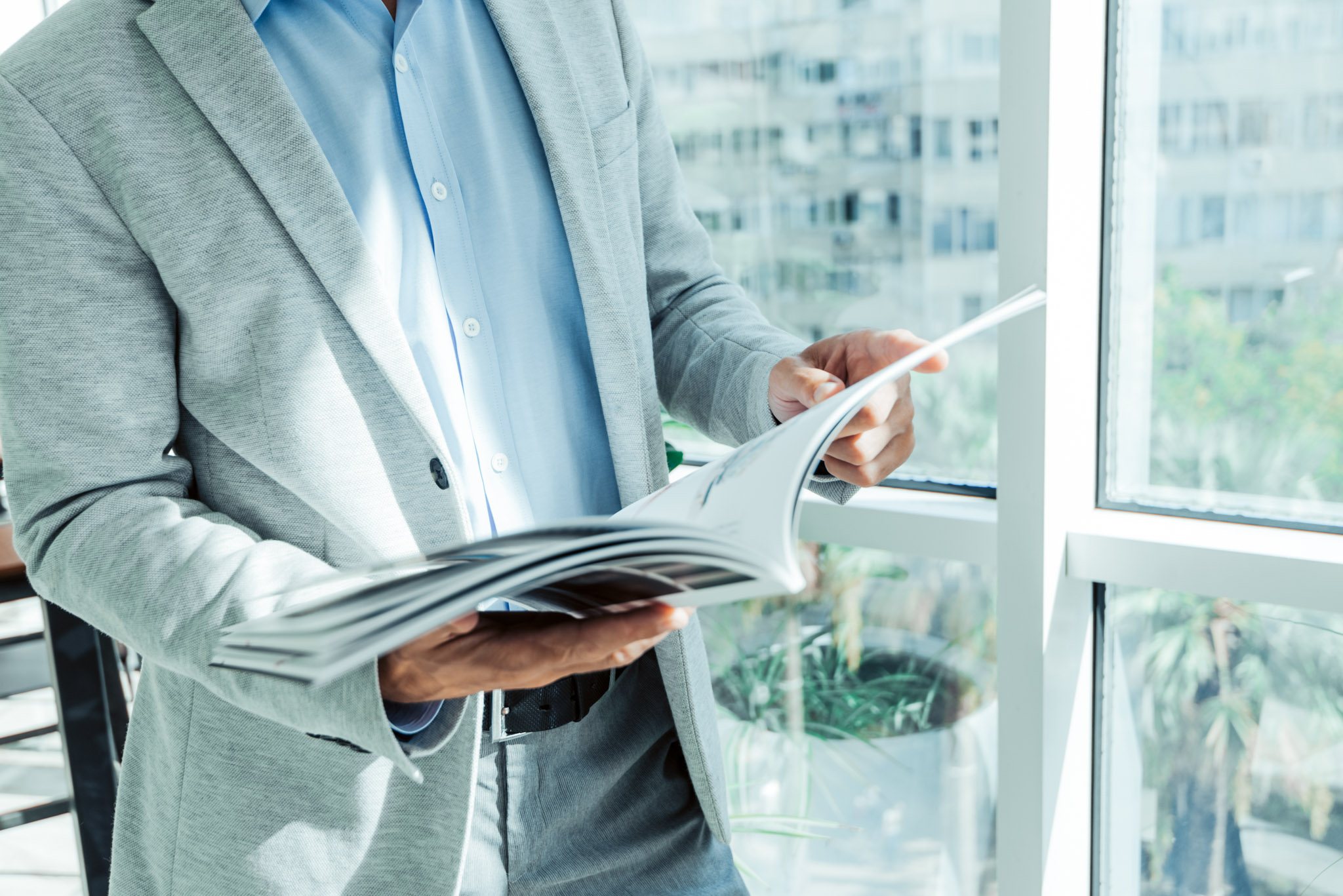 businessman in a business suit reads a magazine near the window with a plant.
