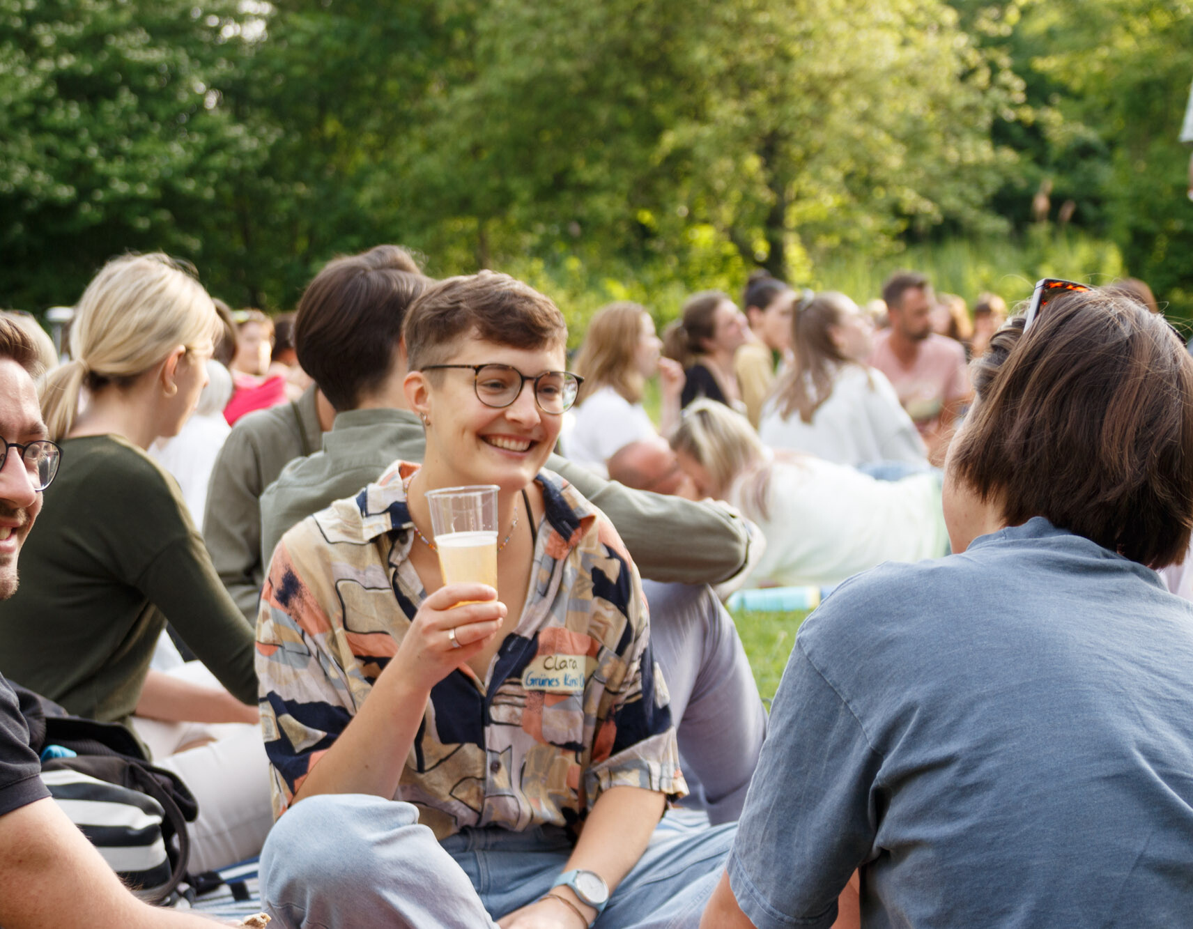 Viele Studierende sitzen im Sommer in der Natur und unterhalten sich.