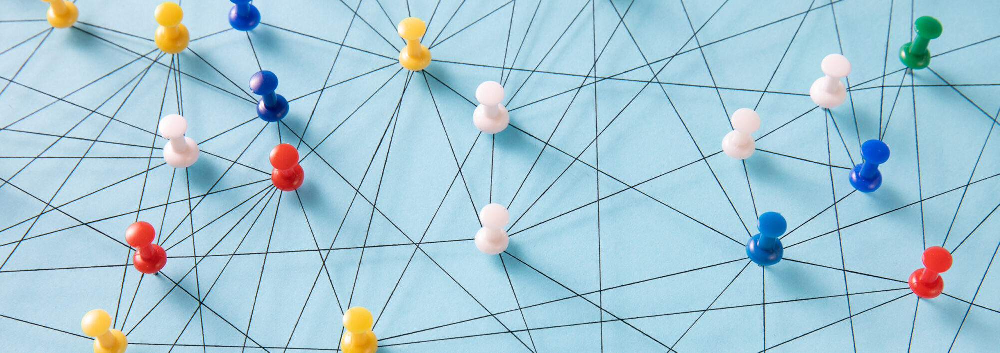An arrangement of colorful pins linked together with string on a pale blue background suggesting a network of connections.