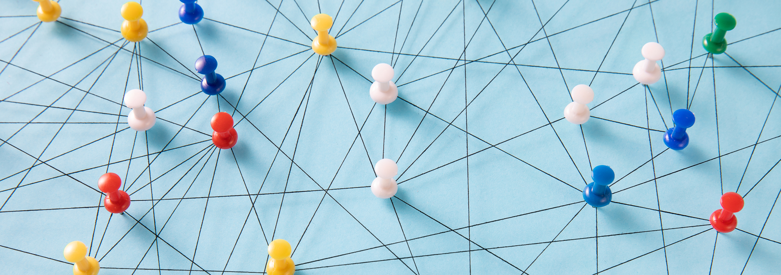 An arrangement of colorful pins linked together with string on a pale blue background suggesting a network of connections.