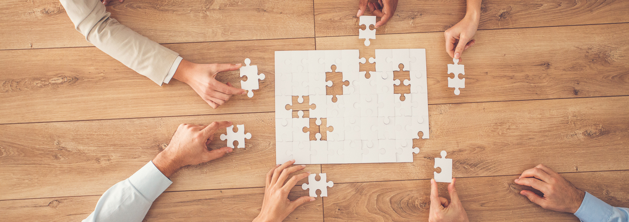 Business people sitting at office desk, putting puzzle pieces together, finding solution, high angle view.