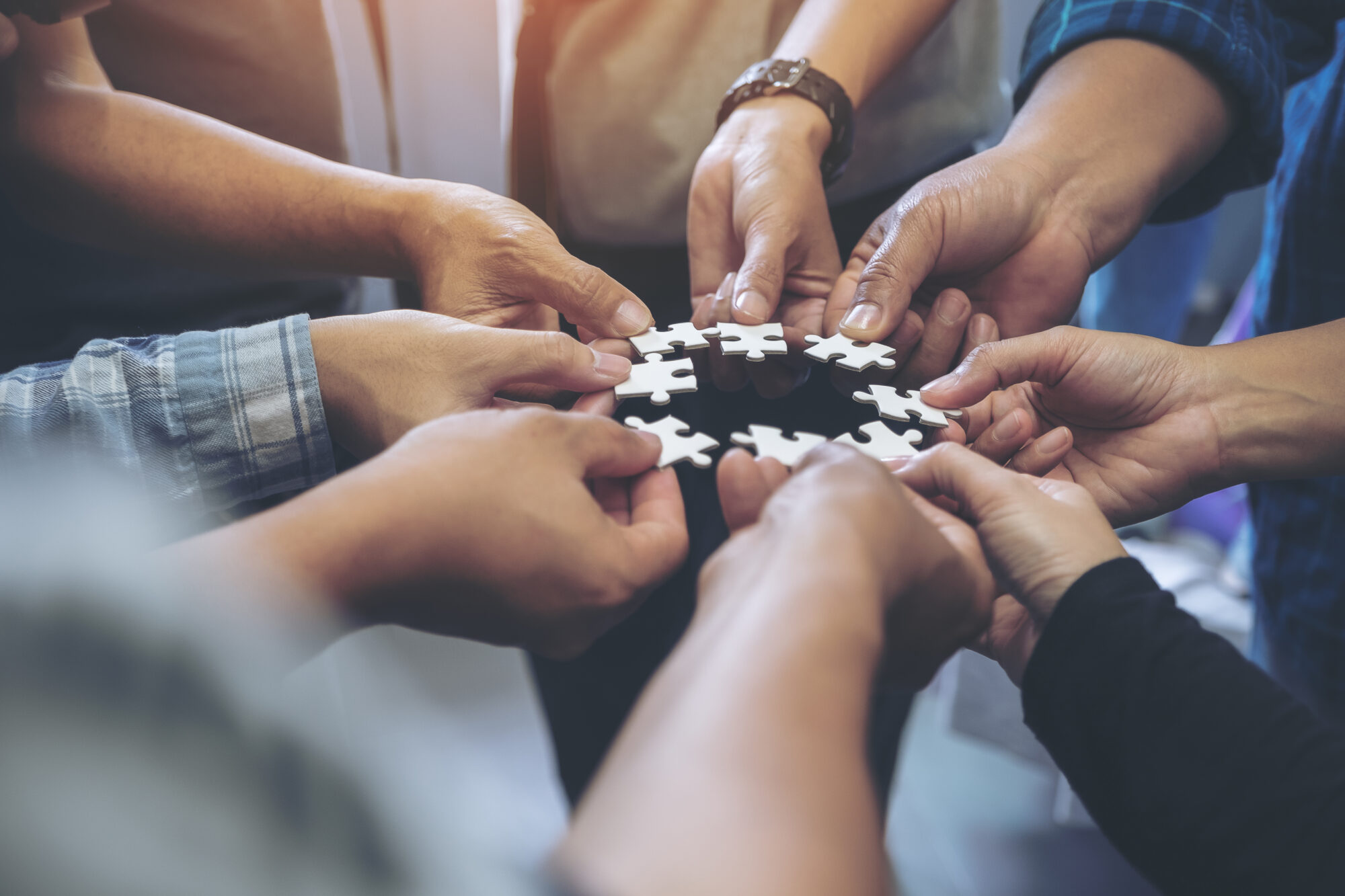 Closeup image of many people hands holding a jigsaw puzzle in circle together