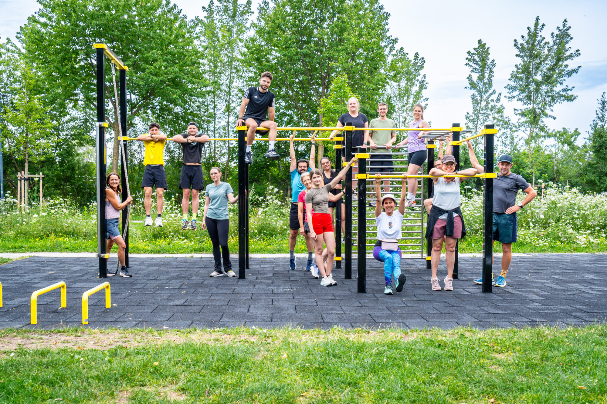 Mitarbeiter*innen und Student*innen posieren f&uuml;r ein Gruppenbild vor einer Calisthenics-Anlage zusammen mit dem ehemaligen Proi-Triathleten Franz H&ouml;fer