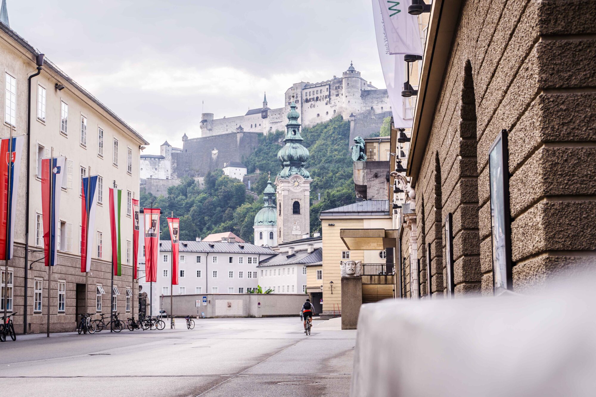 Blick an einem Regentag in die Hofstallgasse mit dem Festspielbezirk, Fahnen und der Festung Hohen Salzburg.