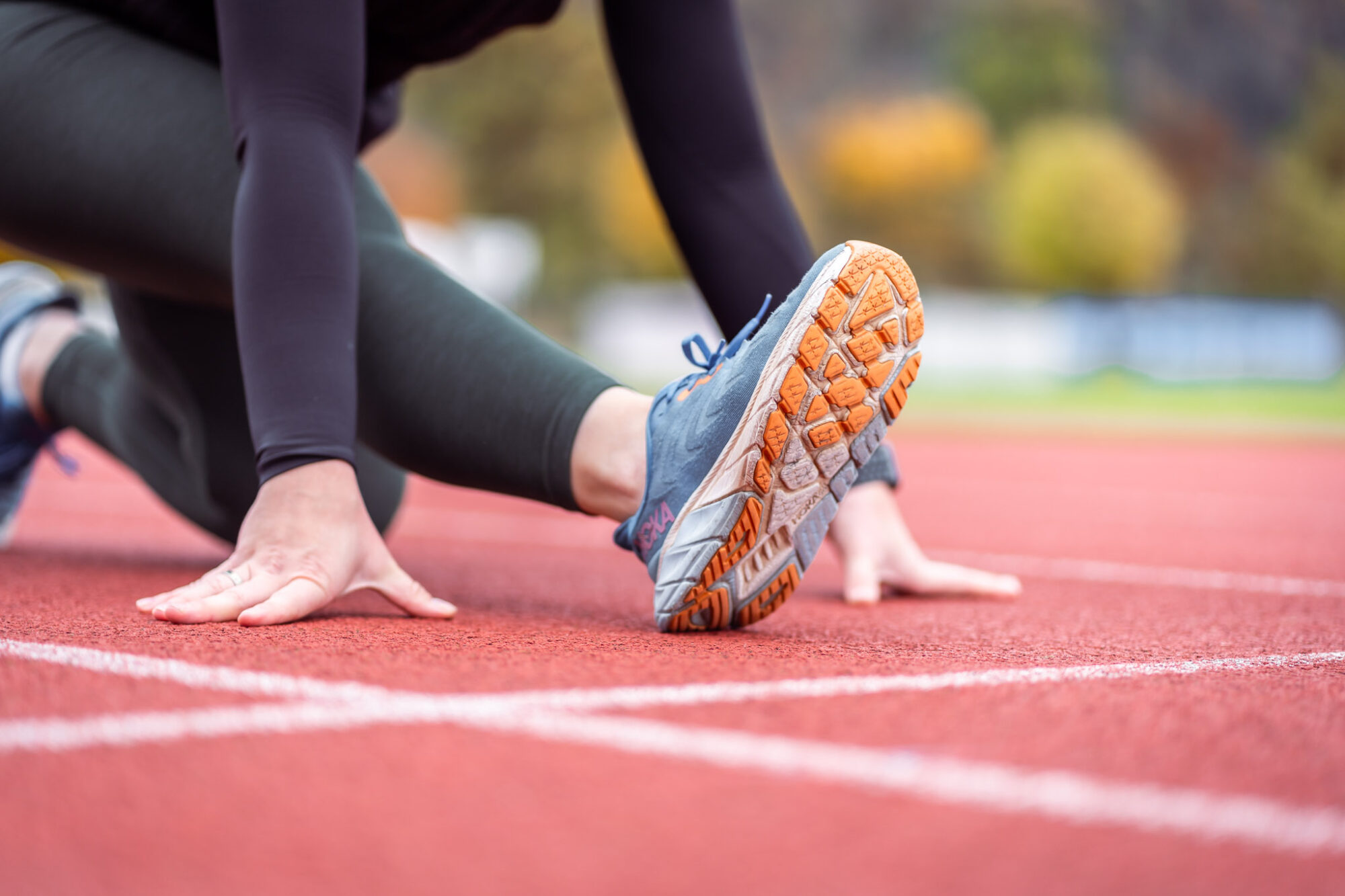 Detailaufnahme einer Sportlerin, die ihr Bein auf einer Laufstrecke dehnt.